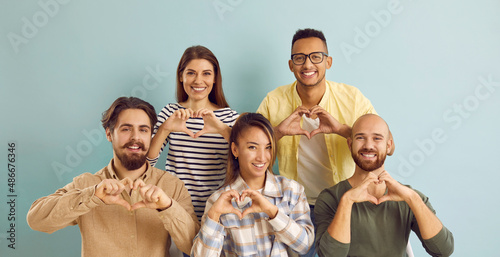 Banner with group portrait of happy smiling thankful diverse multiracial multiethnic people doing heart shape hand gesture on blue color studio background. Love, support, gratitude, kindness concept