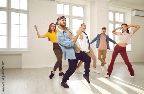 Fototapeta Naklejka Na Ścianę i Meble -  Group of happy young dancers in a modern dance studio. Different cheerful, beautiful, talented people in trendy casual wear enjoying a dancing class, moving to the music and having fun together