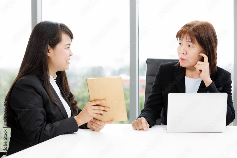 Asian professional successful senior female businesswoman manager in formal suit sitting smiling showing thumb up complimenting happy colleague employee at office working table when job achievement Asian professional successful senior female businesswoman manager in formal suit sitting smiling showing thumb up complimenting happy colleague employee at office working table when job achievement
