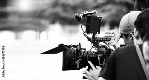 Quadro su tela Back angle view of high definition digital video camera which recording or shooting tv commercial production on pan tilt shift professional head tripod at outdoor location and film crew team with set
