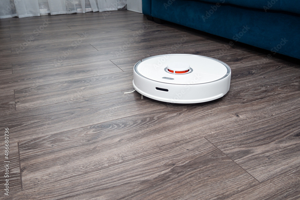a white vacuum cleaner robot on a laminated wooden floor. a white vacuum cleaner robot on a laminated wooden floor.