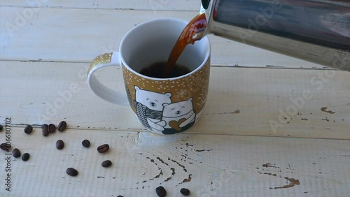 From the coffee maker, black coffee is poured into a cup, scattered coffee beans next to it. Slow motion video. Video reverse