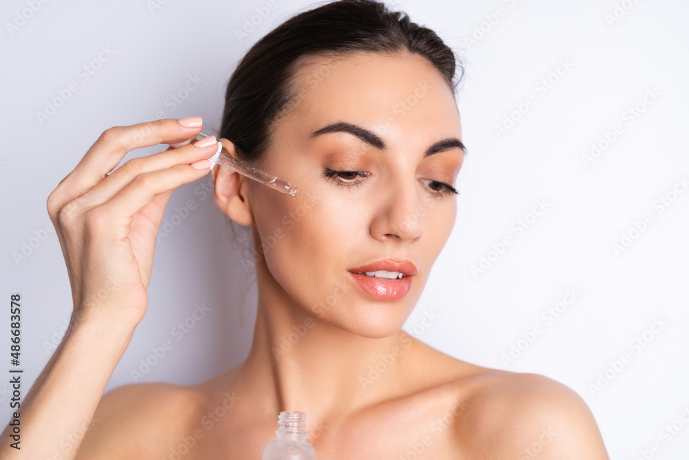 Close beauty portrait of topless woman with perfect skin and natural make-up, holds serum for youth and skin hydration, dropper with cosmetic oil. Close beauty portrait of topless woman with perfect skin and natural make-up, holds serum for youth and skin hydration, dropper with cosmetic oil.