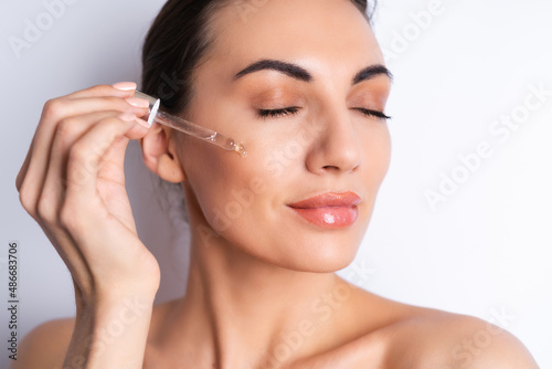 Close beauty portrait of topless woman with perfect skin and natural make-up, holds serum for youth and skin hydration, dropper with cosmetic oil.