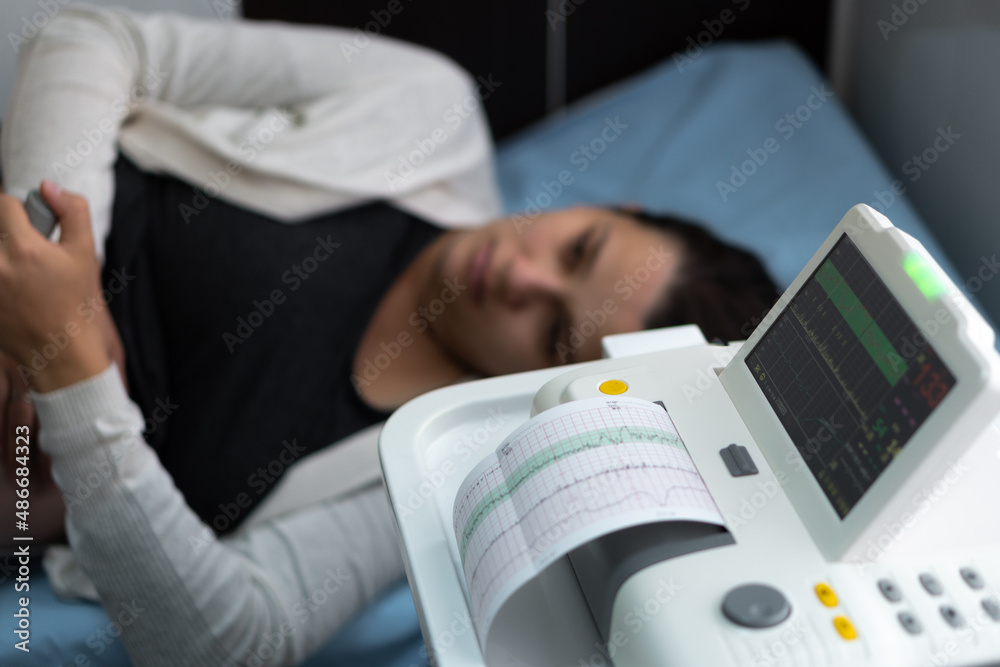 Obraz premium Pregnant Woman On Hospital Couch During Medical Control Cardiotocography. Gynecologist Doctor Hands Turn On Adjust CTG Device Clinic Consultant. Examine Expectant Belly Baby Mother Healthcare Check Up