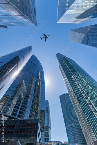 City, skyscrapers, a passenger plane flies over the city. View from the street. Summer 2021