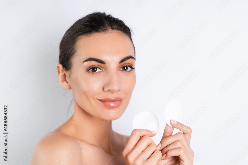 Close beauty portrait of a topless woman with perfect skin and natural makeup removing cotton pads, on a white background. Close beauty portrait of a topless woman with perfect skin and natural makeup removing cotton pads, on a white background.