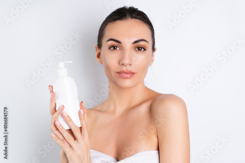Close beauty portrait of a topless woman with perfect skin and natural makeup holding bottle of shampoo, body lotion, on a white background.