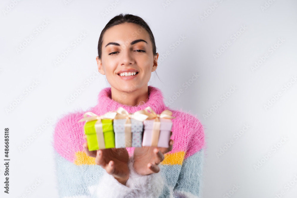 Young cheerful girl in a soft colored sweater on a white background holds small cute gift boxes Young cheerful girl in a soft colored sweater on a white background holds small cute gift boxes