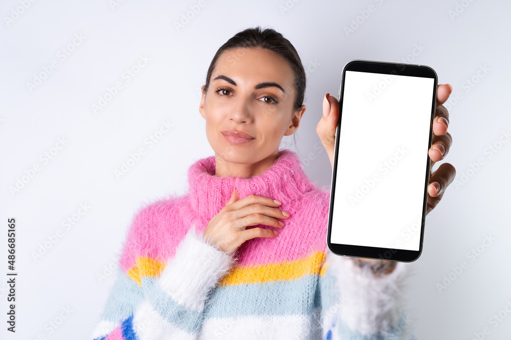 Obraz premium Young cheerful girl in a bright colored sweater on a white background holds a big phone in focus with a blank white screen