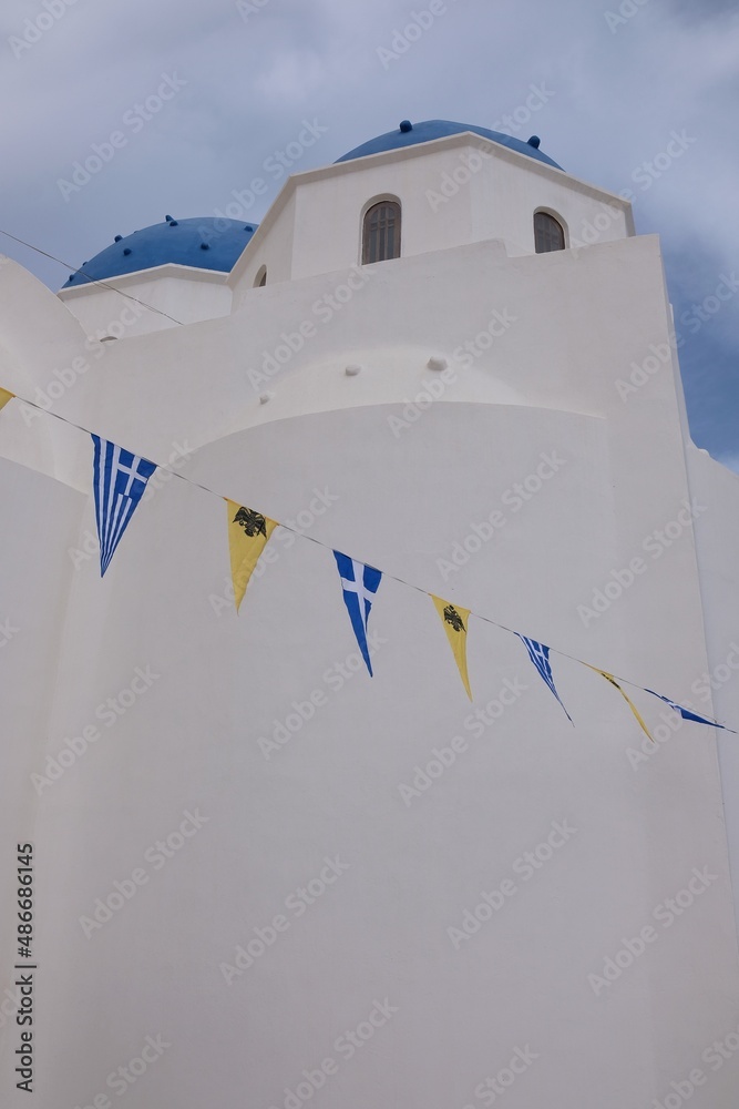 View of a whitewashed orthodox church with byzantine and greek flags in Santorini Greece 