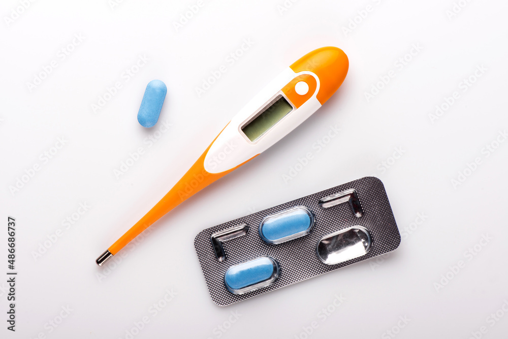 Electronic thermometer and pills on white background