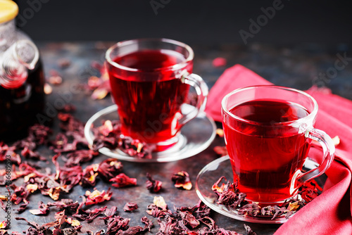 Hibiscus tea in glass cup and a burgundy napkin. Cup of hibiscus tea and dry hibiscus petals on a dark background. Healthy natural slimming drink