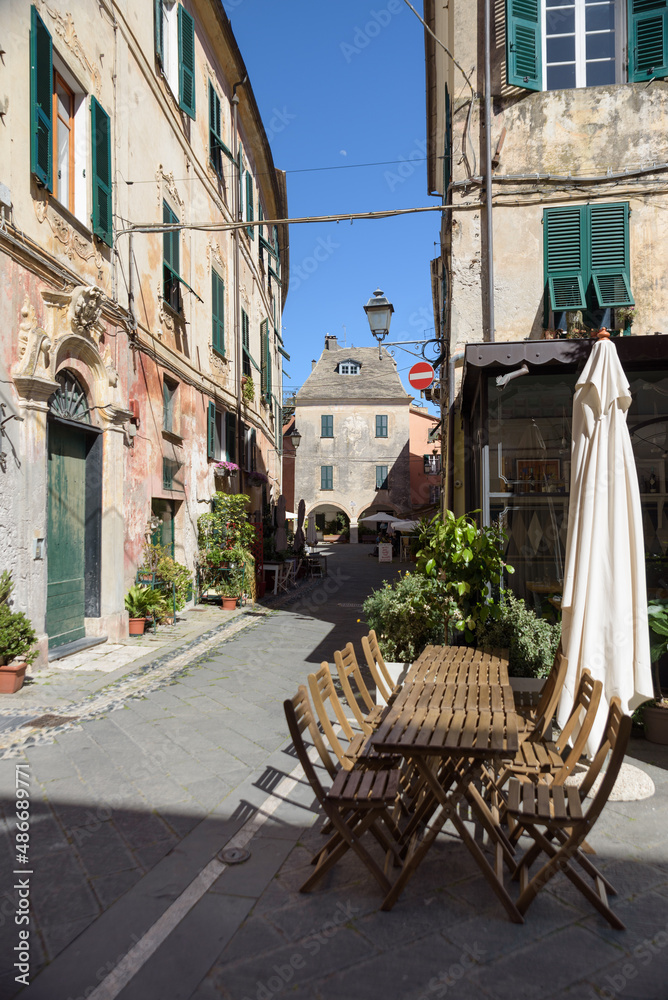 Finalborgo, Finale Ligure, Italy. May 5, 2021. In a small street, wooden tables outside a restaurant in Piazza del Tribunale. In the distance, Piazza Aicardi.