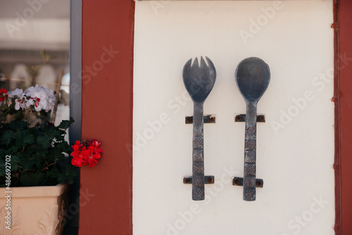 Photos Large metal and old spoon and fork with carvings and patterns on them hang on the wall of cafe or restaurant on Santorini island, Oia, Greece