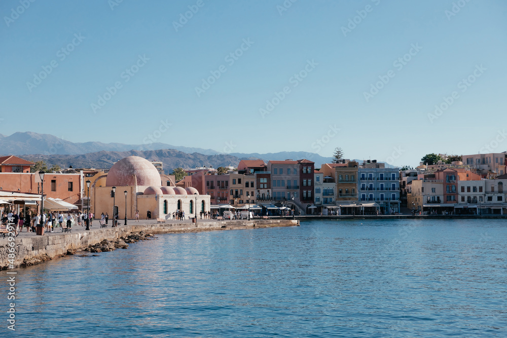 Colorful buildings and Mosque in the old Venetian harbor of Chania town on Crete island, Greece. Janissaries or Kioutsouk Hassan Mosque. Turkish mosque with mountains on background. Copy space