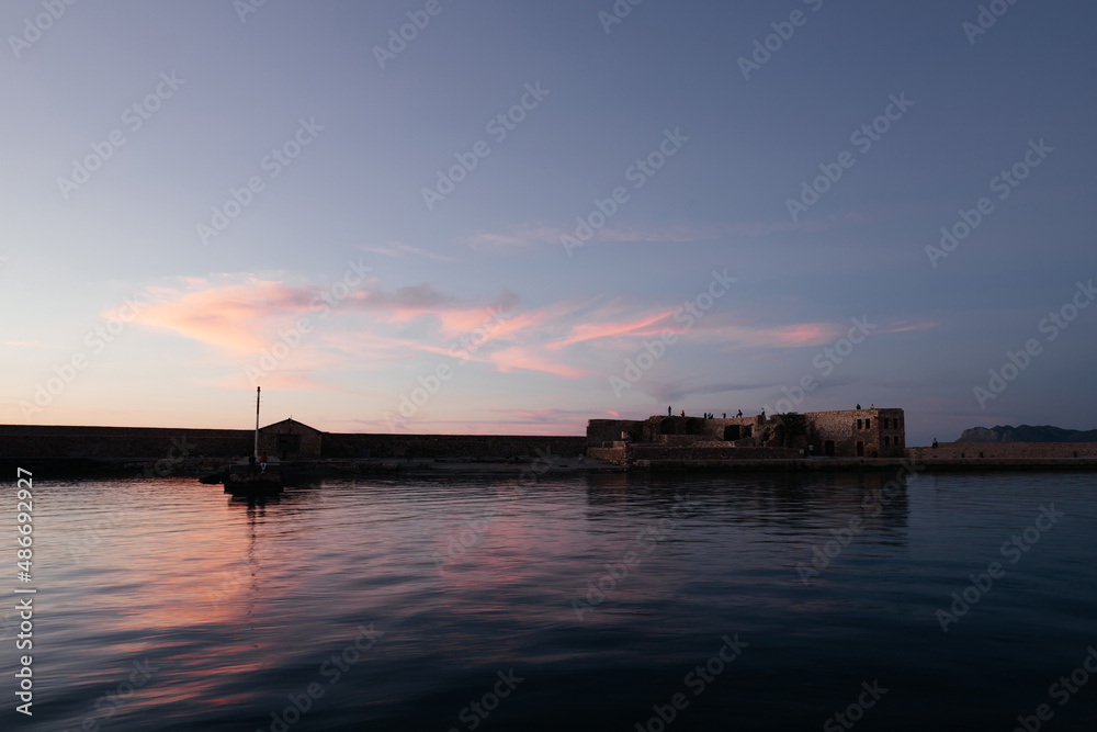 Venetian harbour near lighthouse in old harbour of Chania with nice sunset reflection on water of sea; Crete; Greece. Long exposure. People watching sunset from the harbour. Nice background.