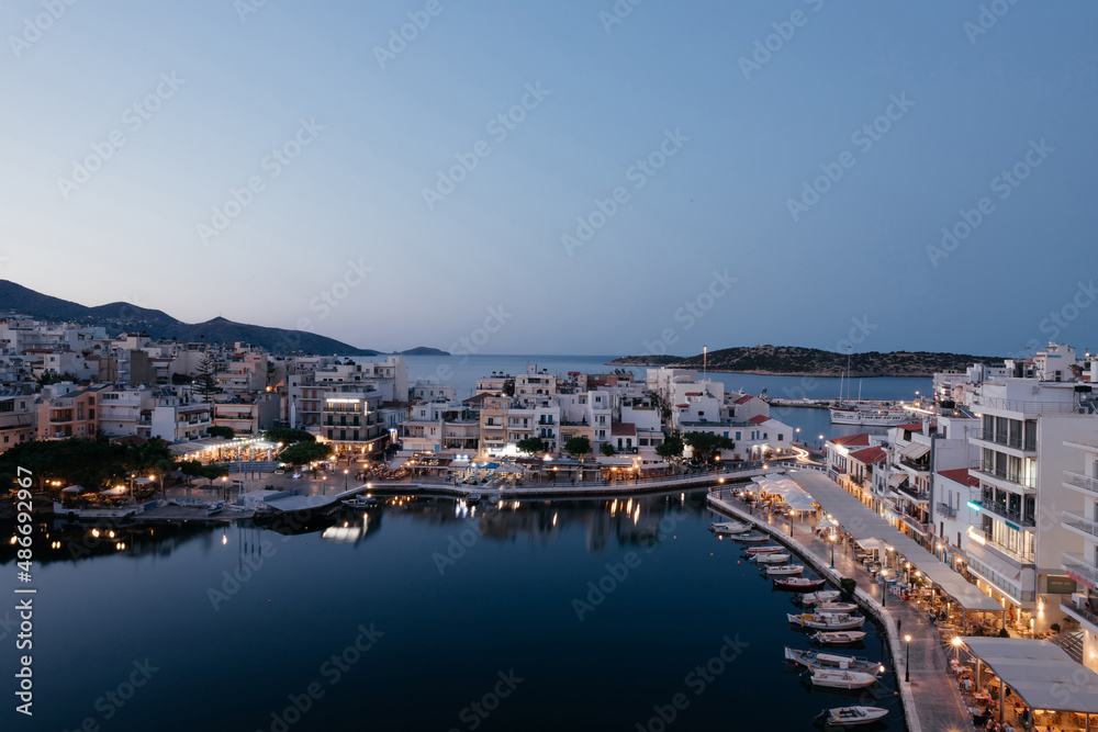 Beautiful view of small town Agios Nikolaos and Voulismeni lake in Crete island, Greece. Place with busy tourist life on the waterfront with cafe and restaurants, boats and mountains on background.