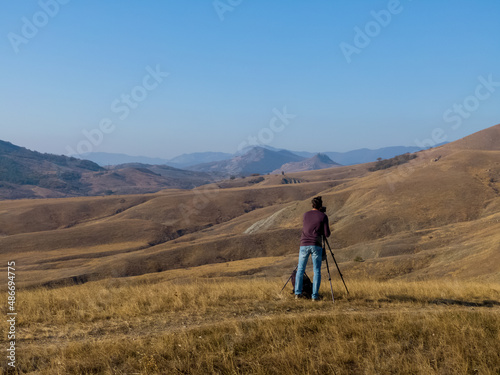 A man with a camera on a tripod and a backpack against the background of mountain parallax