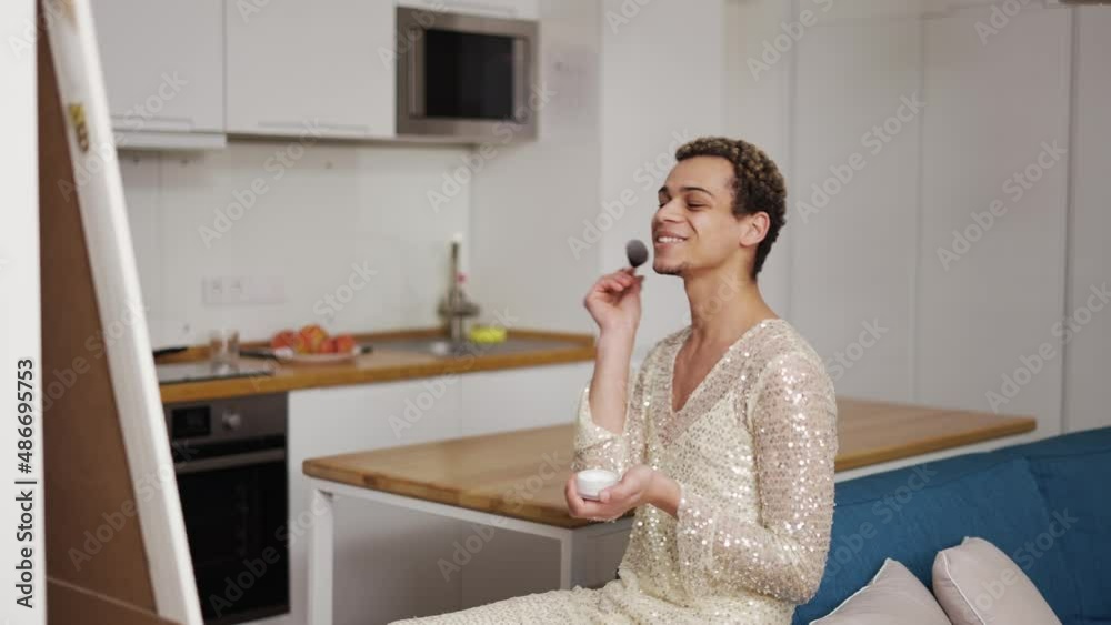 A transgender guy in fancy dress doing make up with brush and powder A transgender guy in fancy dress doing make up with brush and powder