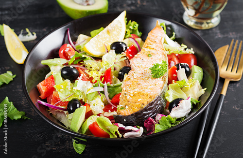 Baked salmon fish fillet and fresh green lettuce, tomato, avocado and black olives. Greek salad.