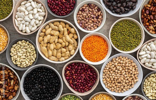 Different types of legumes in bowls, green with yellow peas and mung beans, chickpeas and peanuts, colored beans and lentils, top view