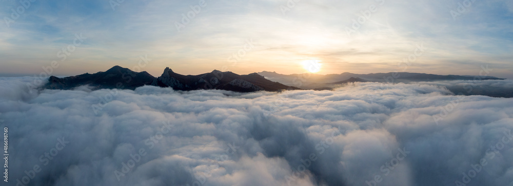 Panorama Sunset over a mountain range covered with dense fog. Delightful landscape. Aerial view