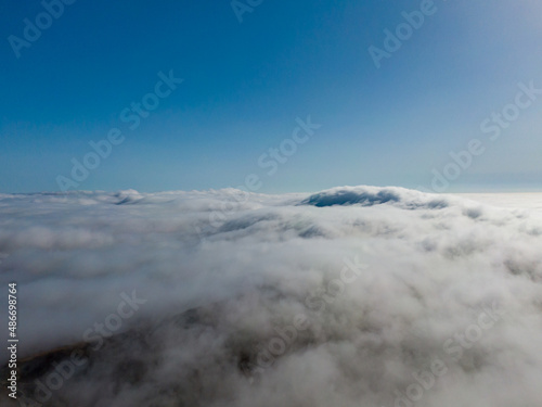 Aerial view of a dense fog lying on the hills under a clear blue sky