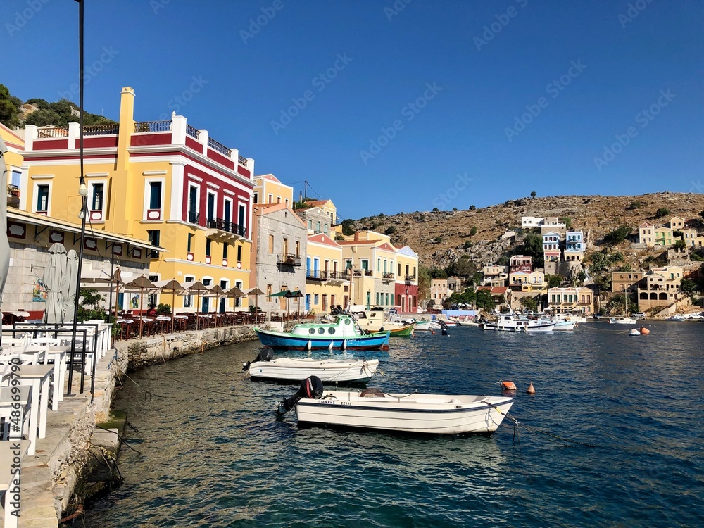 Symi island and Aegean sea view. On of small Greek Dodecanese islands. Small marina with boats and yachts. Aegean Sea and island view. Turquoise blue water, colourful buildings, small boats mooring by