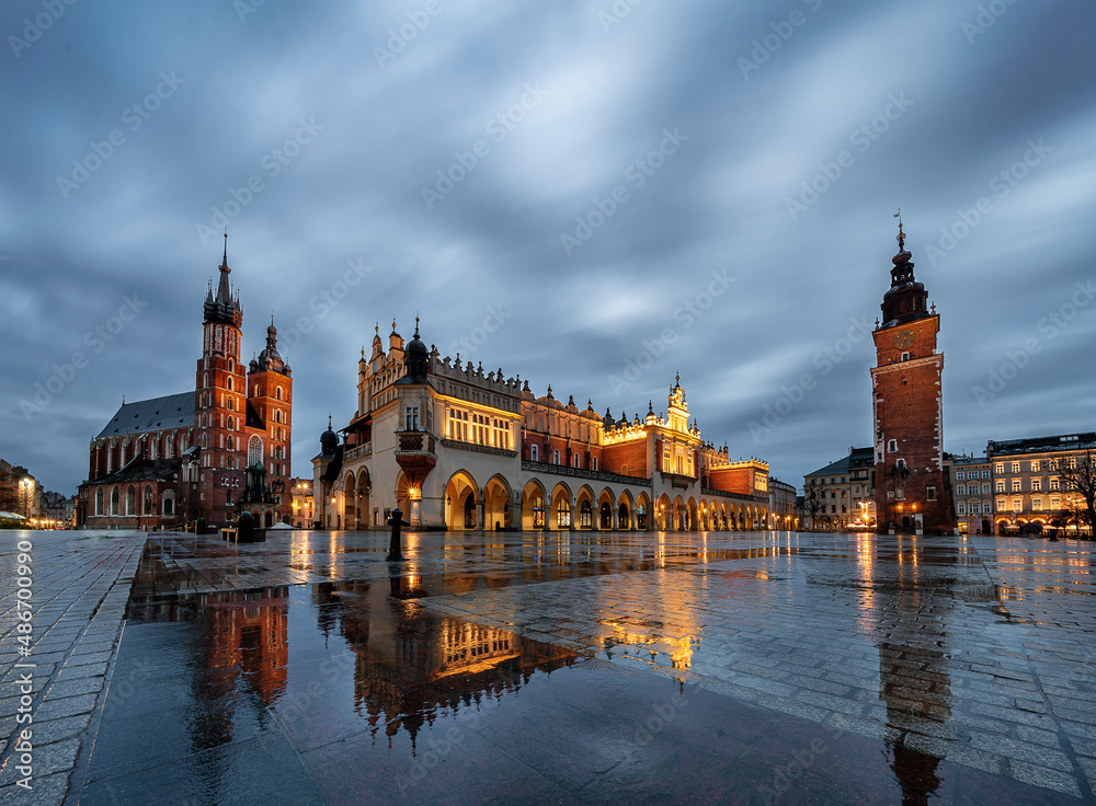 Krakow main square with reflections of St mary's basilica and the cloth hall during rainy sunrise
