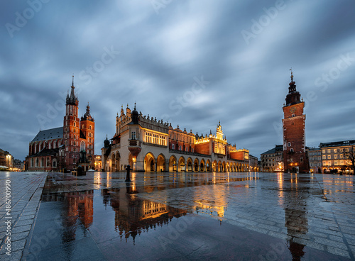 Krakow main square with reflections of St mary's basilica and the cloth hall during rainy sunrise