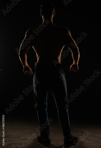 Silhouette of topless guy posing from the back in studio while flexing