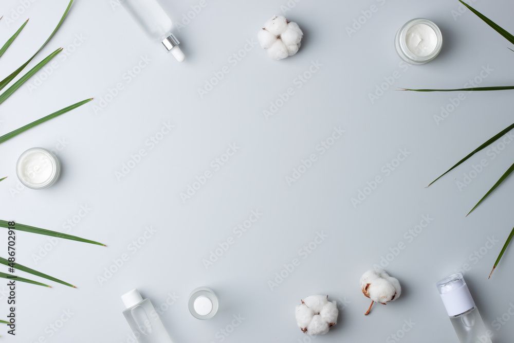Cosmetic skin care products with flowers and palm leaf on grey background. Flat lay, copy space Cosmetic skin care products with flowers and palm leaf on grey background. Flat lay, copy space