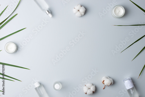 Cosmetic skin care products with flowers and palm leaf on grey background. Flat lay, copy space
