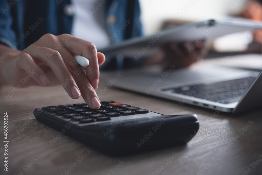 Business woman using calculator to calculate financial report, working at office with laptop computer on table Business woman using calculator to calculate financial report, working at office with laptop computer on table