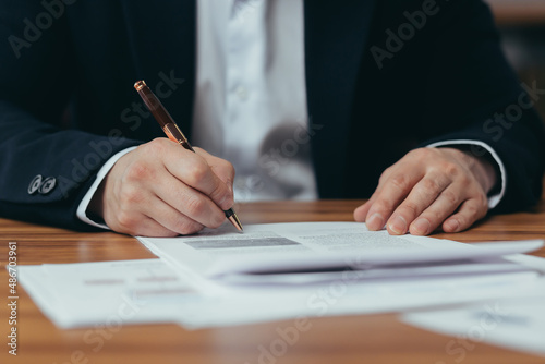 Close-up photo of Asian businessman's hands signing bank documents, man working in modern office, sitting at table, banker's paperwork © Liubomir