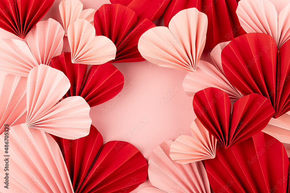 Holiday Valentine day background with frame of heap pink and red paper folded ribbed hearts on soft light pink background as festive backdrop, top view, copy space.