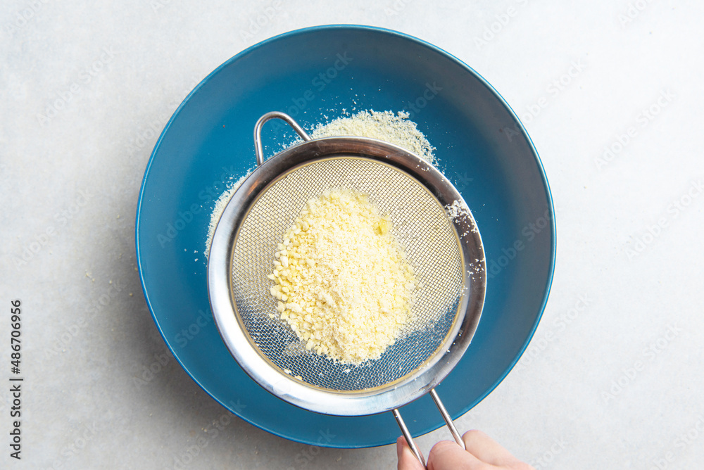 almond flour is sifted through a sieve into a blue bowl on a background of concrete. concept for a recipe for making almond flour. top view almond flour is sifted through a sieve into a blue bowl on a background of concrete. concept for a recipe for making almond flour. top view