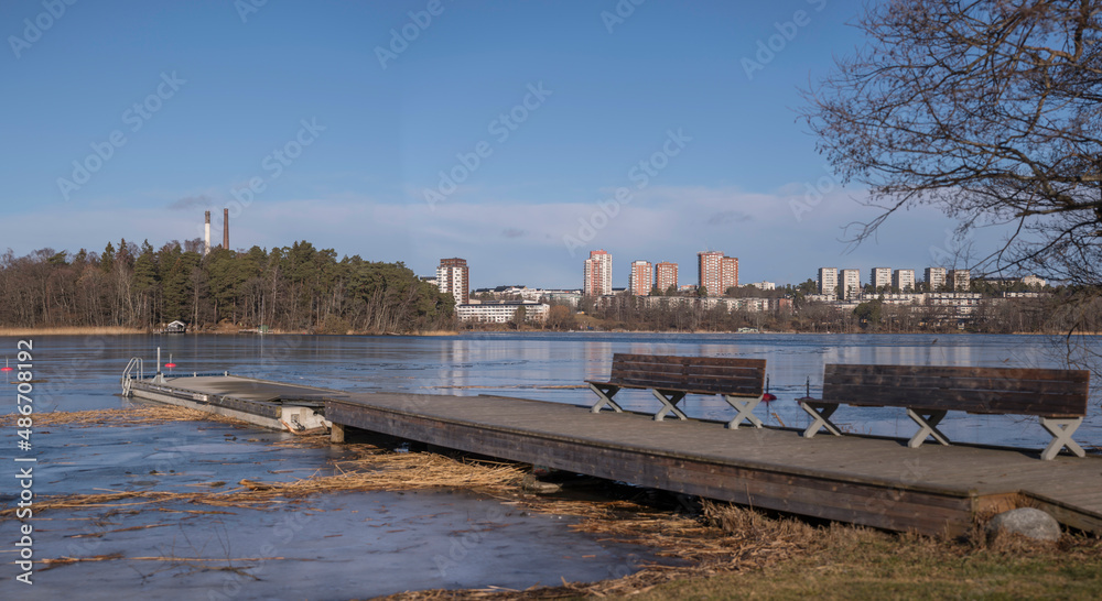 Panorama view over the waterfront at the district Hässelby from the island Lovö at a jetty with benches in the icy lake Mälaren a sunny winter day in Stockholm