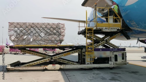 A worker is loading a cargo containers from the freighter airplane at the airport. In the logistic industry the air transport is very popular.