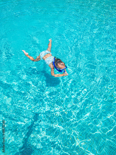 Little cute girl at the swimming pool wearing a diving mask, snorkel equipment. Top aerial view. Summer vacation holiday toddler girl swimming in amazing ocean lagoon