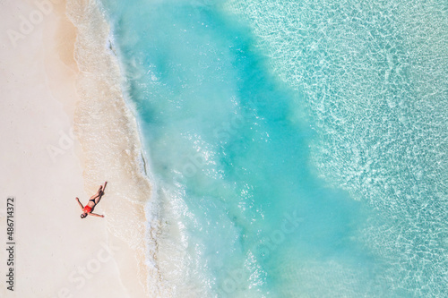 Aerial view of a woman relaxing on tropical beach Maldives islands. Vacation adventure aerial beach landscape, turquoise water, soft sand. Amazing top view from drone beach shore azure lagoon seaside photo