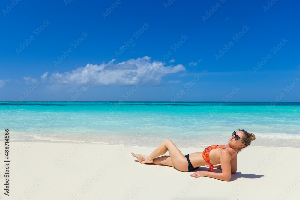 Fashion woman portrait in bikini on tropical beach. Relaxing summer mood, calm waves on sandy beach, exotic tropical island landscape with woman relaxing in the sand, sunglasses and sexy swimwear Fashion woman portrait in bikini on tropical beach. Relaxing summer mood, calm waves on sandy beach, exotic tropical island landscape with woman relaxing in the sand, sunglasses and sexy swimwear