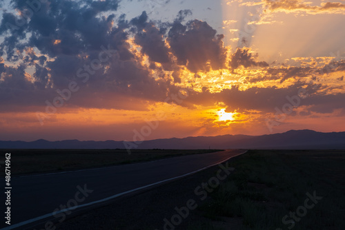 Fototapeta Naklejka Na Ścianę i Meble -  Beautiful sunset with cloudy sky and sun rays. Sunrise with road, mountains silhouettes and orange golden clouds.