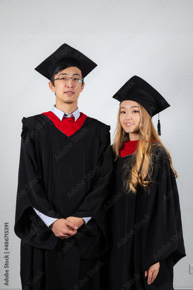 Graduates couple in gowns posing together on white background Graduates couple in gowns posing together on white background