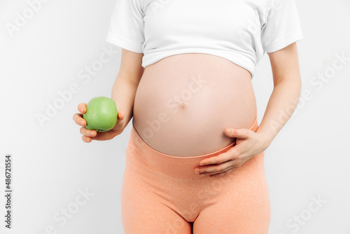 pregnant woman holding a green apple on a white background. Expectant mother is expecting a baby, eating fruit at home