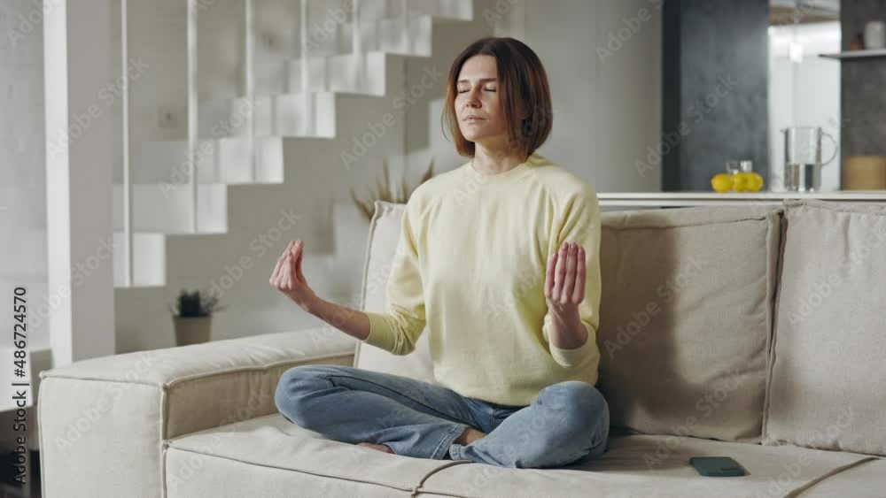Woman meditating in lotus position on comfy couch Woman meditating in lotus position on comfy couch