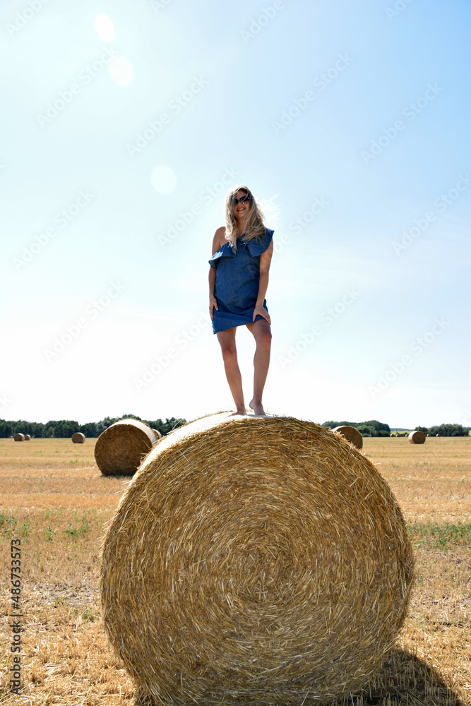 Young woman in sunglasses smiling stands on a round haystack in a cereal field Young woman in sunglasses smiling stands on a round haystack in a cereal field