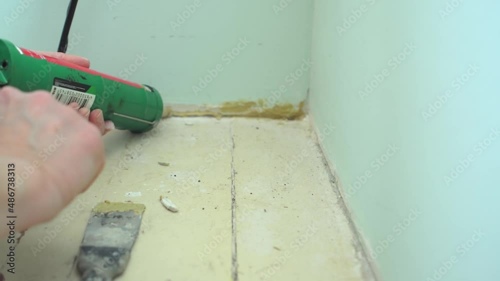 Closeup of female worker hand closes hole between wall and floor with silicone sealant caulking