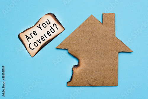 Text on burned paper house model on blue background. Home insurance concept.